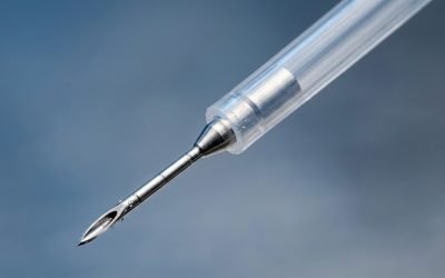 Extreme close-up of a fine sclerotherapy injection needle with a beveled metal tip emerging from a clear catheter sheath.