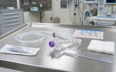 A clinician's gloved hands using a graduated measuring device beside a low-profile PEG feeding button and purple Y-port connector on a surgical tray, preparing a replacement tube.