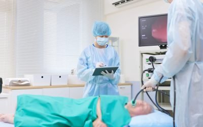 Two clinicians in protective gear preparing an endoscope in a procedure room with a monitor