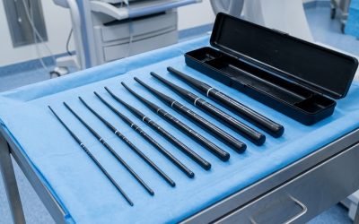 A set of long, tapered esophageal dilation dilators arranged in graduated sizes on a blue sterile drape over a stainless-steel procedure tray, beside their open black storage case in a procedure room.