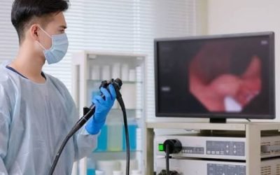 Masked clinician in scrubs holding an endoscope next to a monitor displaying the endoscopic view