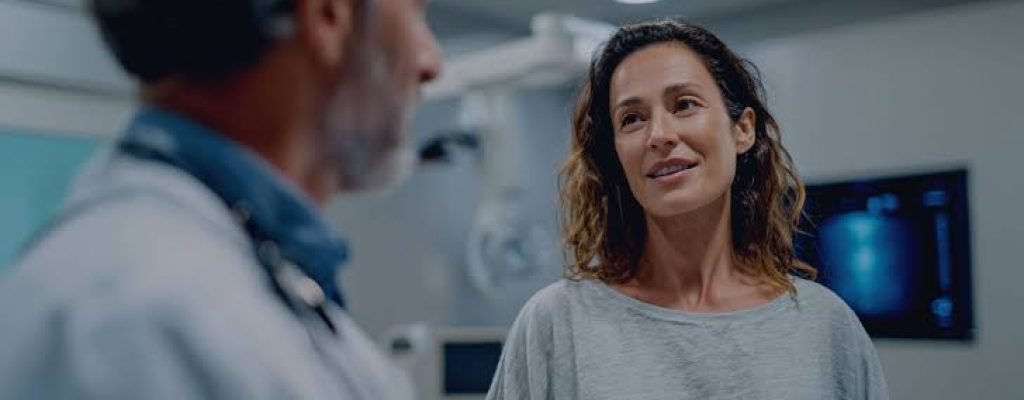 Male doctor in a white coat talking with a female patient in a clinic examination room